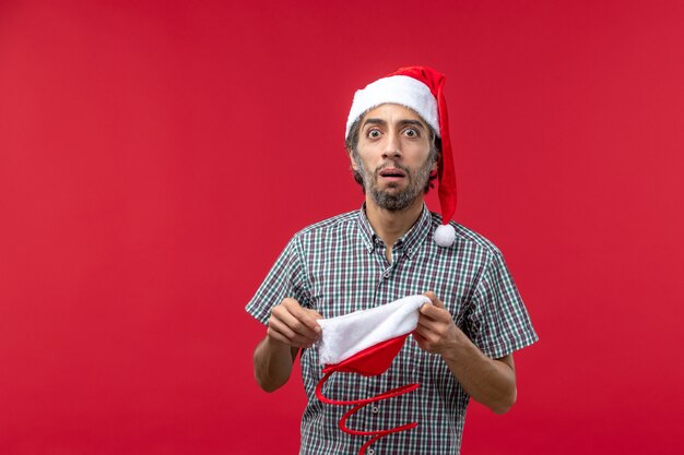 Front view of young man with christmas toy cap on red wall