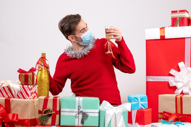 Free photo front view young man with mask looking at champagne sitting around xmas gifts