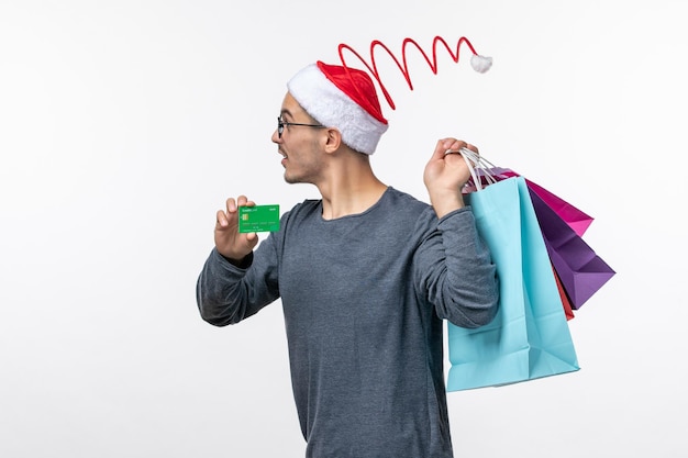 Front view of young man with packages and bank card on a white wall