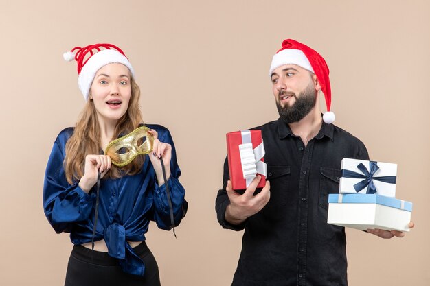 Front view of young man with pretty woman holding presents and mask on pink wall