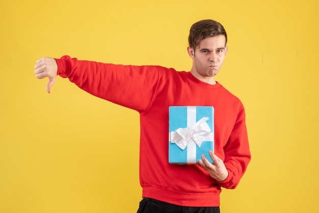 Free photo front view young man with red sweater making thumb down sign on yellow background