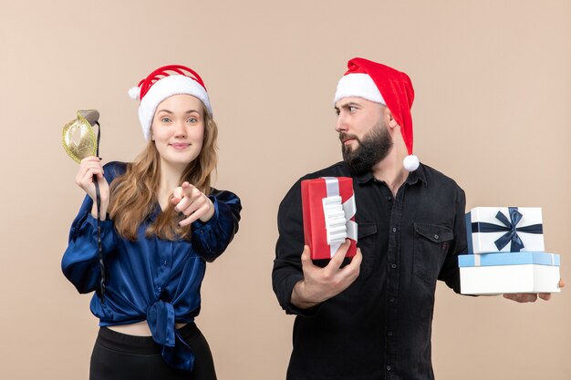 Front view of young man with woman holding presents and mask on pink wall