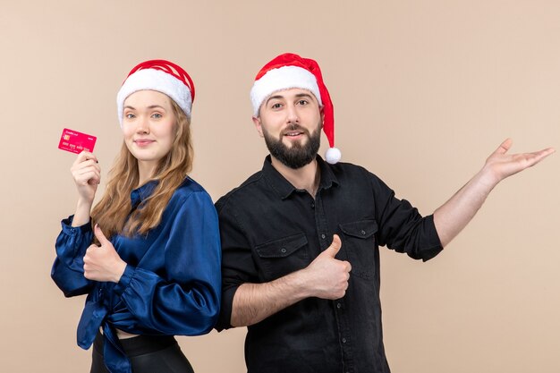 Front view of young man with woman who's holding bank card on pink wall