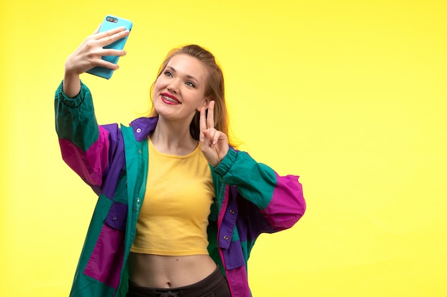 Free Photo a front view young modern woman in yellow shirt black trousers and colorful jacket taking a selfie on the phone happy expression