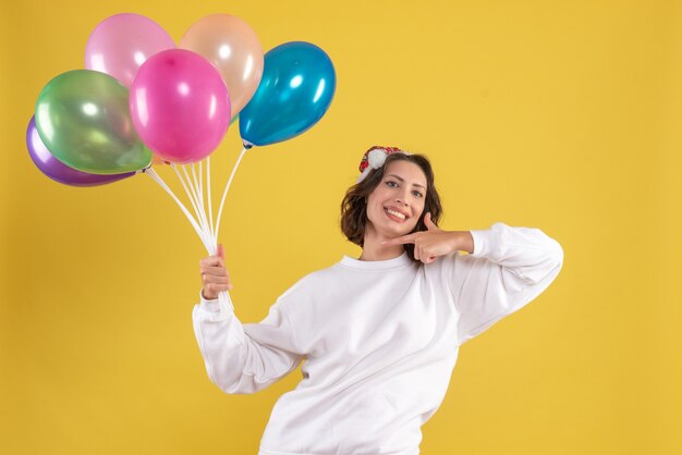 Front view young pretty female holding balloons on yellow color christmas woman new year emotion