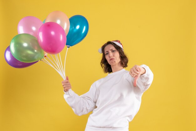 Front view young pretty female holding colorful balloons on yellow color christmas new year emotions woman