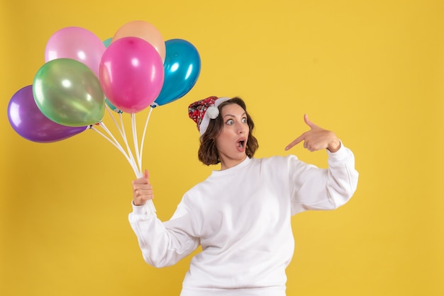 Front view young pretty female holding colorful balloons on yellow emotions christmas new year woman color