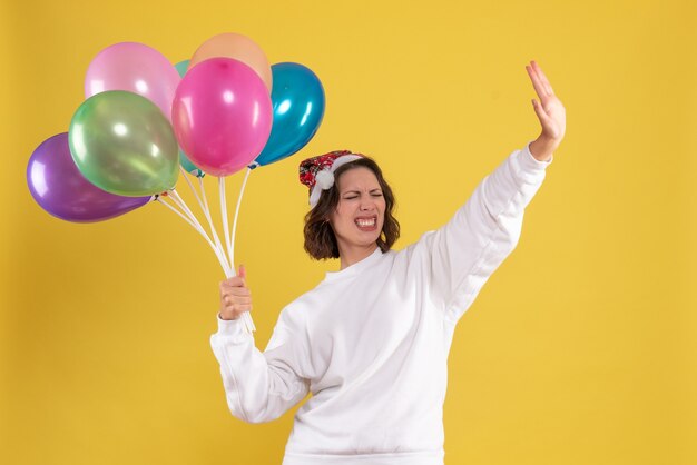 Front view young pretty female holding colorful balloons on a yellow new year emotion christmas woman color