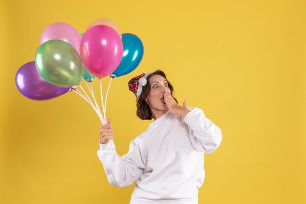 Front view young pretty female holding colorful balloons on yellow new year emotion christmas woman color