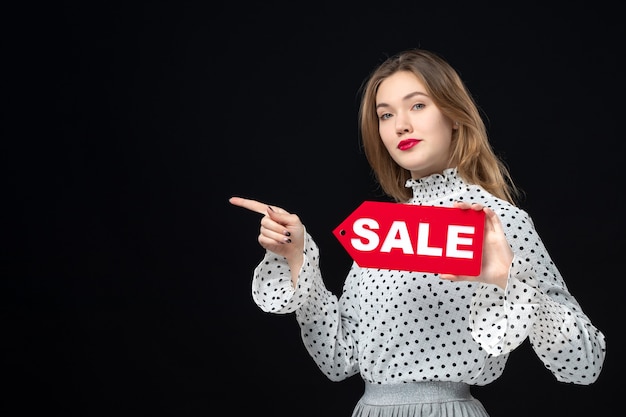 Free photo front view young pretty female holding sale writing on a black wall color shopping fashion photo woman emotion red