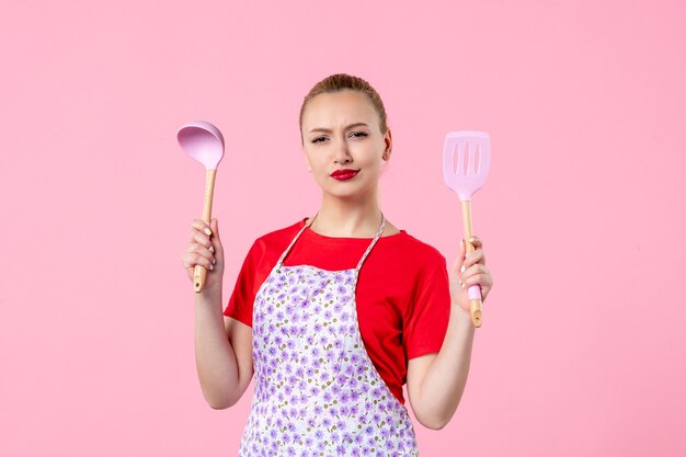 Front view young pretty housewife in cape with spoons on pink wall