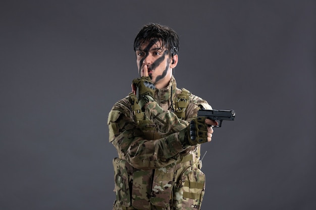 Free photo front view of young soldier in camouflage with gun on a dark wall