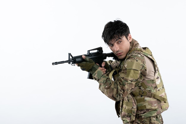 Free photo front view young soldier fighting in camouflage with machine gun white wall