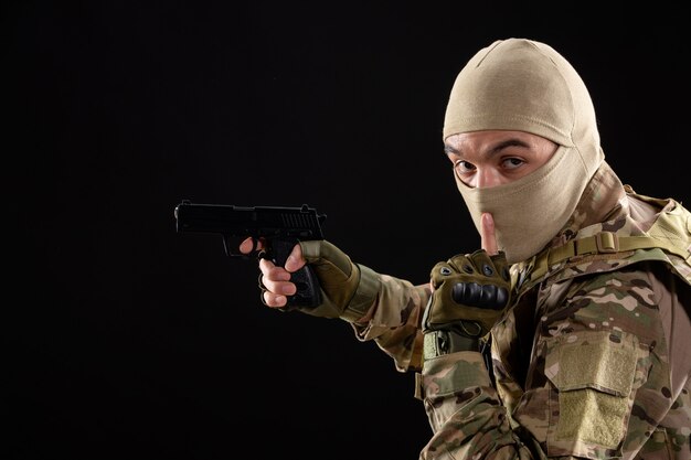 Front view young soldier in uniform aiming gun on black wall