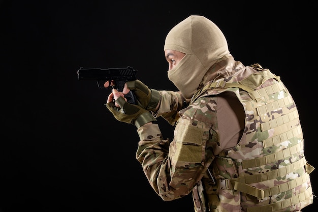 Free photo front view young soldier in uniform aiming gun on black wall