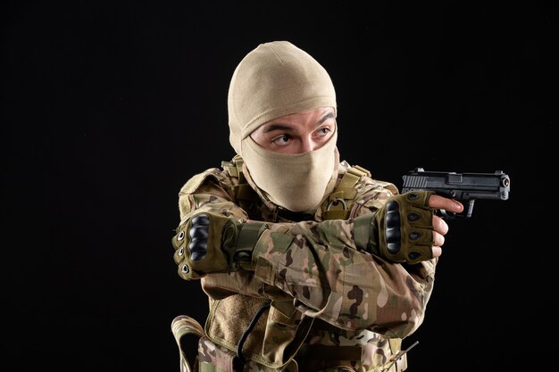 Front view of young soldier in uniform aiming gun on black wall