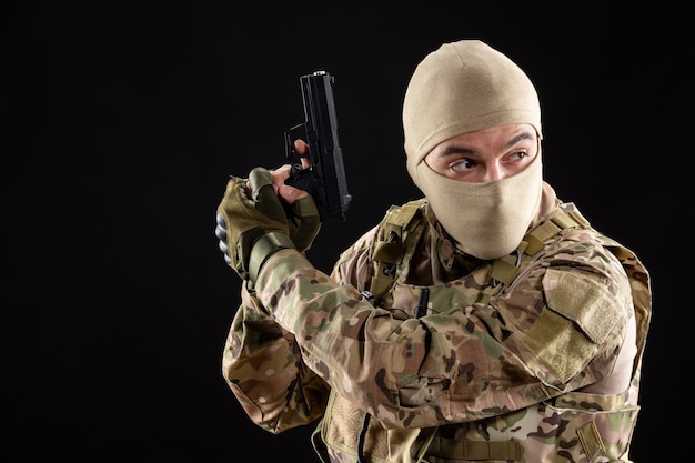 Front view of young soldier in uniform aiming gun on black wall