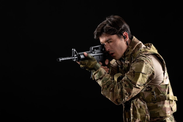 Free Photo front view young soldier in uniform aiming his rifle on black wall