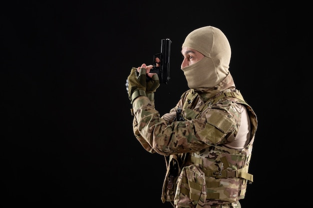 Front view young soldier in uniform with gun on black wall