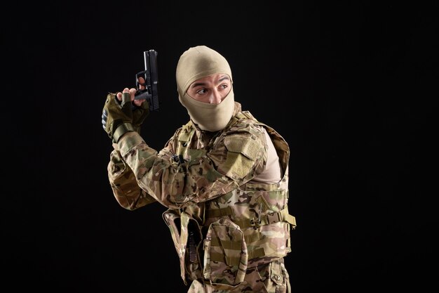 Front view young soldier in uniform with gun on black wall