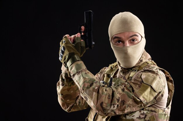 Front view of young soldier in uniform with gun on black wall