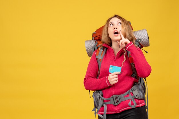 Front view of young thinking travelling girl in medical mask collecting her luggage holding bank card looking up