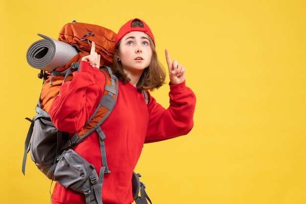 Front view young traveller woman in red backpack pointing fingers up