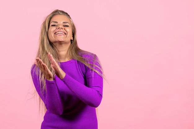 Front view of young woman in beautiful purple dress posing on a pink wall