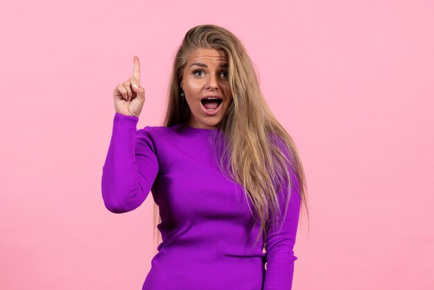 Front view of young woman in beautiful purple dress posing on the pink wall