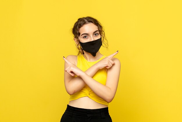 Front view of young woman in black mask on yellow wall