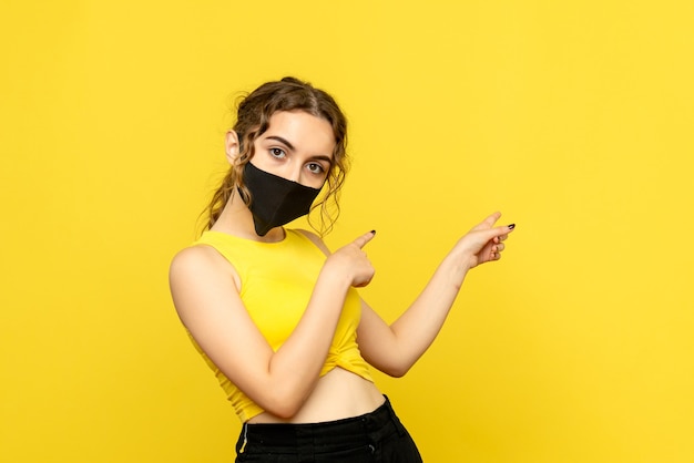 Front view of young woman in black mask on yellow wall