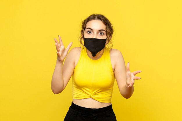 Front view of young woman in black mask on yellow wall