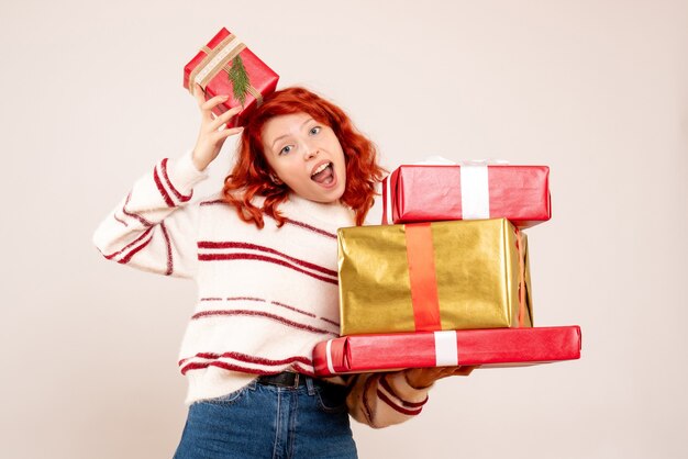 Front view of young woman carrying christmas presents on a white wall