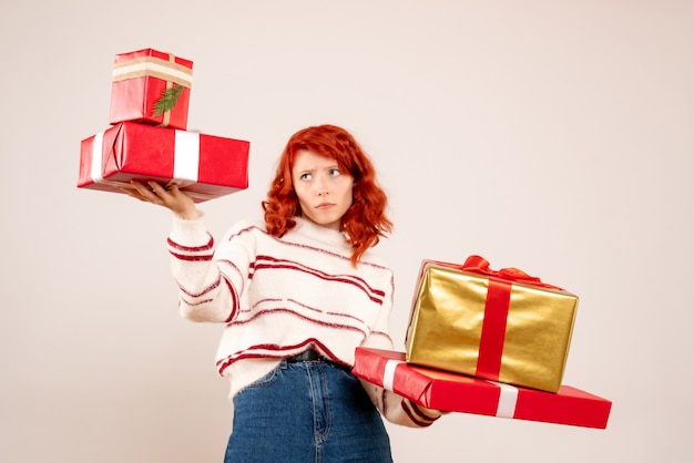 Front view of young woman carrying christmas presents on the white wall