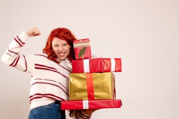 Front view of young woman carrying christmas presents on white wall