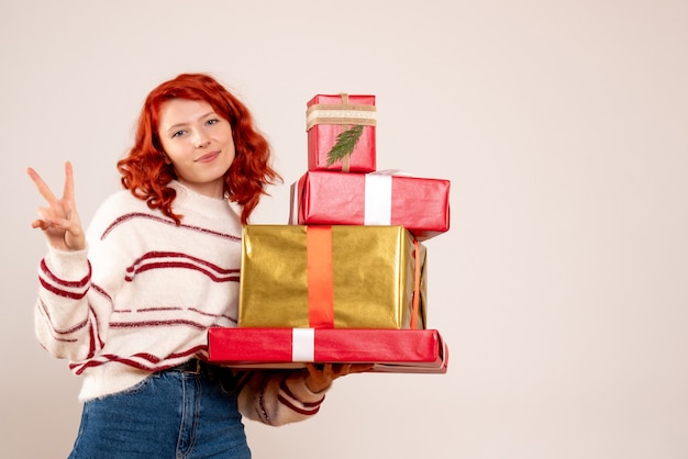 Front view of young woman carrying christmas presents on white wall