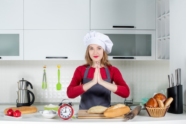 Front view young woman in cook hat and apron joining hands together in the kitchen