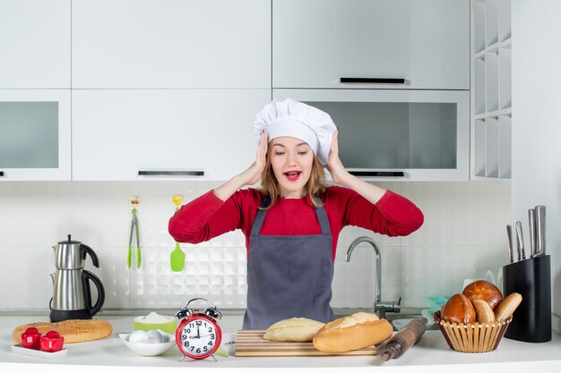 Front view young woman in cook hat and apron showing her surprise in the kitchen