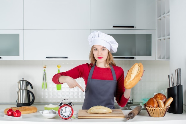 Front view young woman in cook hat holding bread in the kitchen