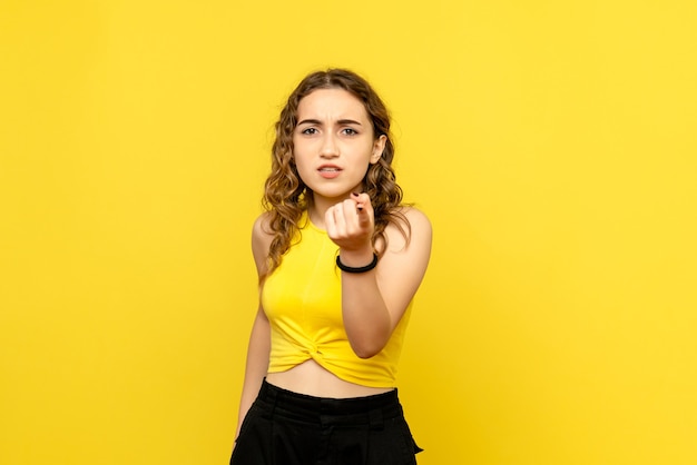 Front view of young woman feeling confused on yellow wall