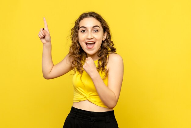 Front view of young woman feeling excited on yellow wall