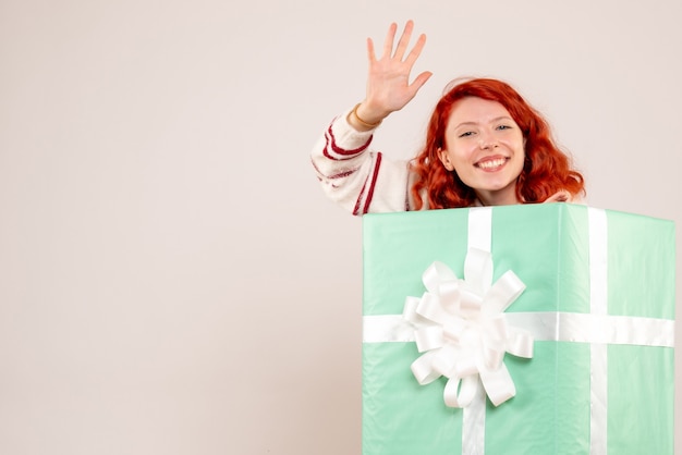 Front view of young woman hiding inside christmas present on a white wall