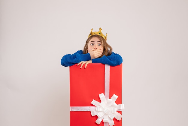 Front view of young woman hiding inside present box on the white wall