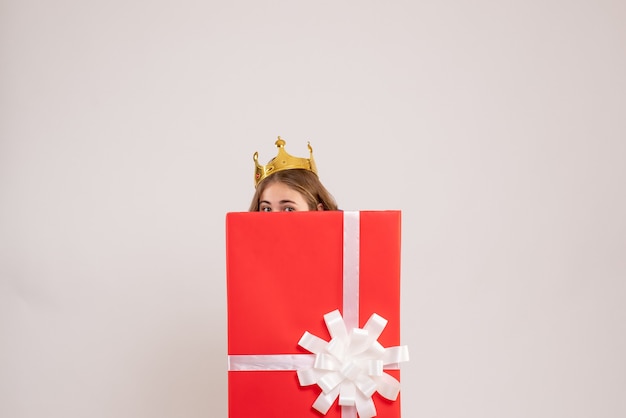 Front view of young woman hiding inside present box on white wall