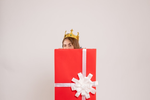 Front view of young woman hiding inside present box on white wall