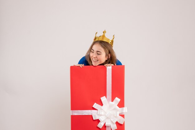 Front view of young woman hiding inside present box on white wall