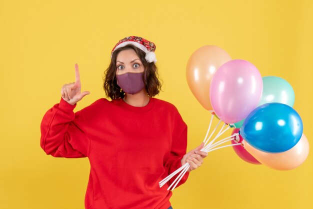 Front view young woman holding balloons in mask on a yellow virus covid party emotion new year color woman