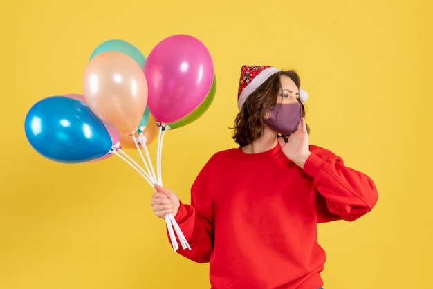 Front view young woman holding balloons in mask on yellow