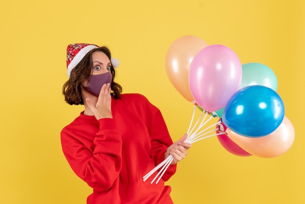 Front view young woman holding balloons in mask on yellow