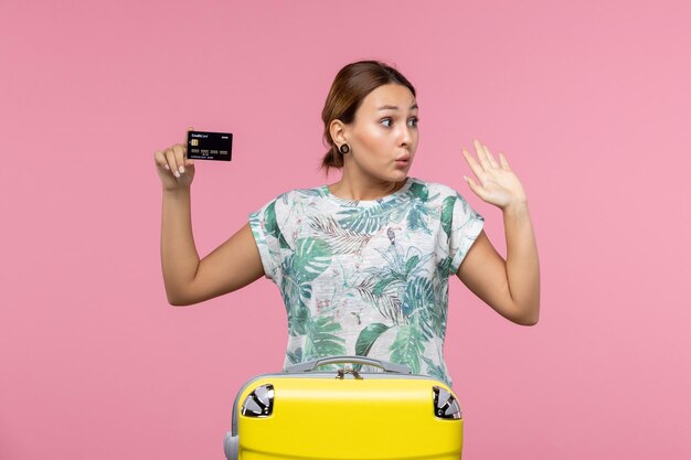 Front view of young woman holding black bank card on pink wall